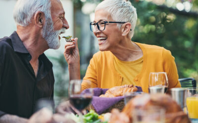 Playful senior woman feeding her husband on a garden party